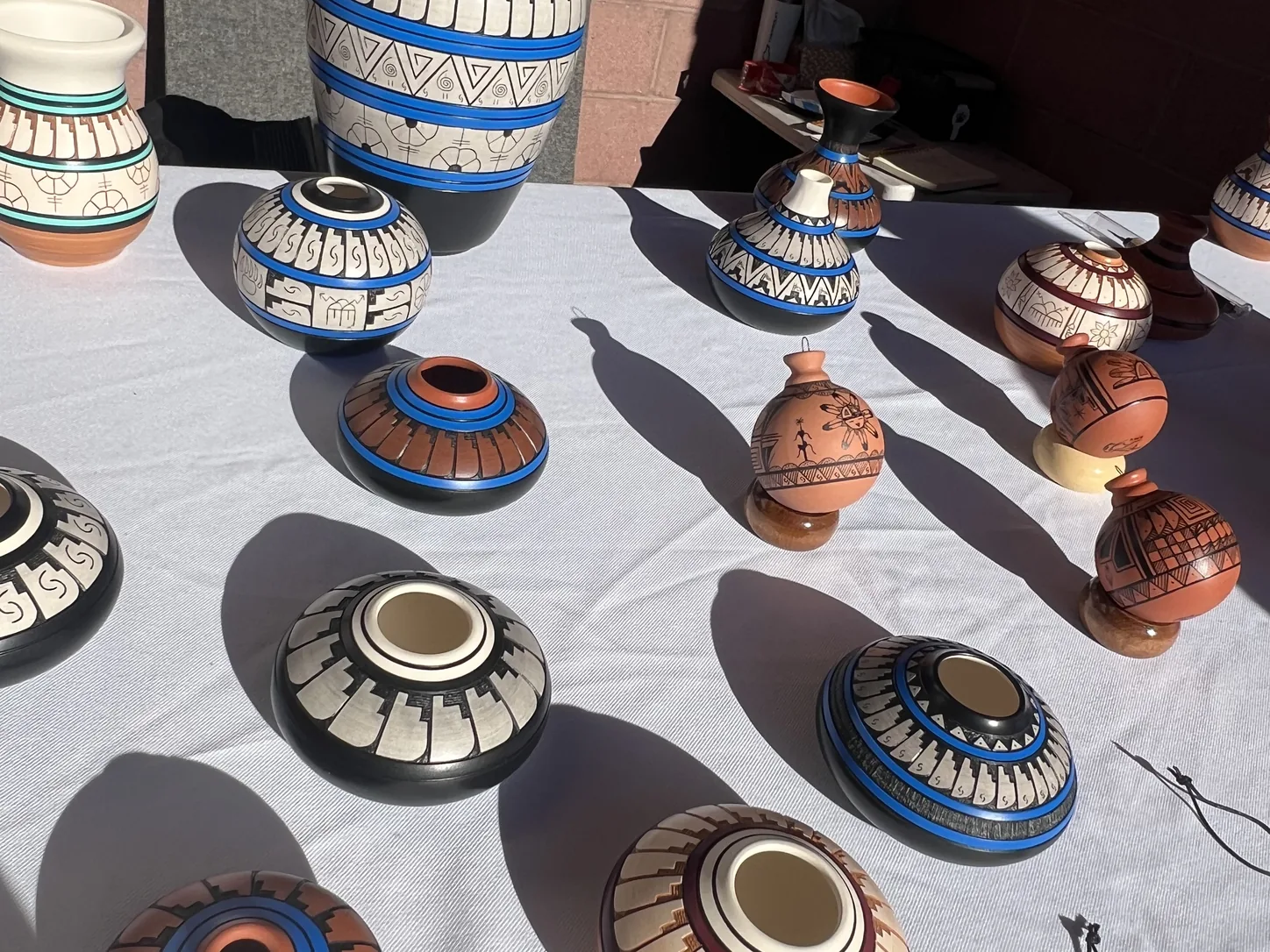 Poteries navajo et hopi peintes à la main, disposées en rangées sur une nappe blanche sur la table d’un vendeur au monument : jarres et bols en noir, blanc, bleu et terre cuite